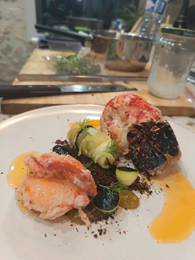 Queue et pince de homard, rouleau de courgette et sauce orange, cuisine en arrière-plan