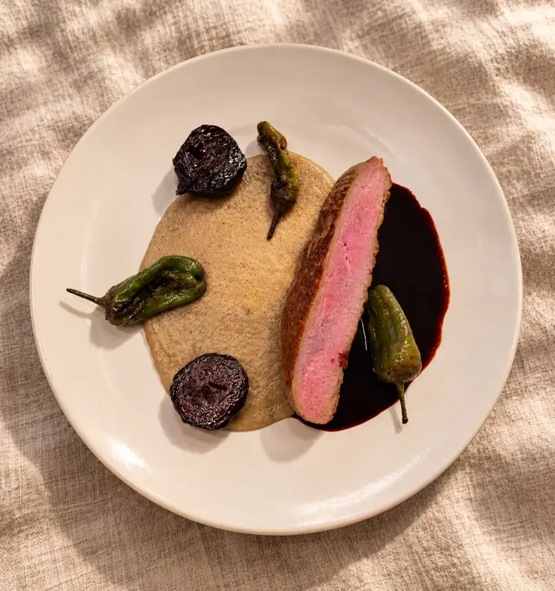 Tranche de viande rosée, purée crème, poivrons verts et betteraves sur une assiette crème posée sur du lin