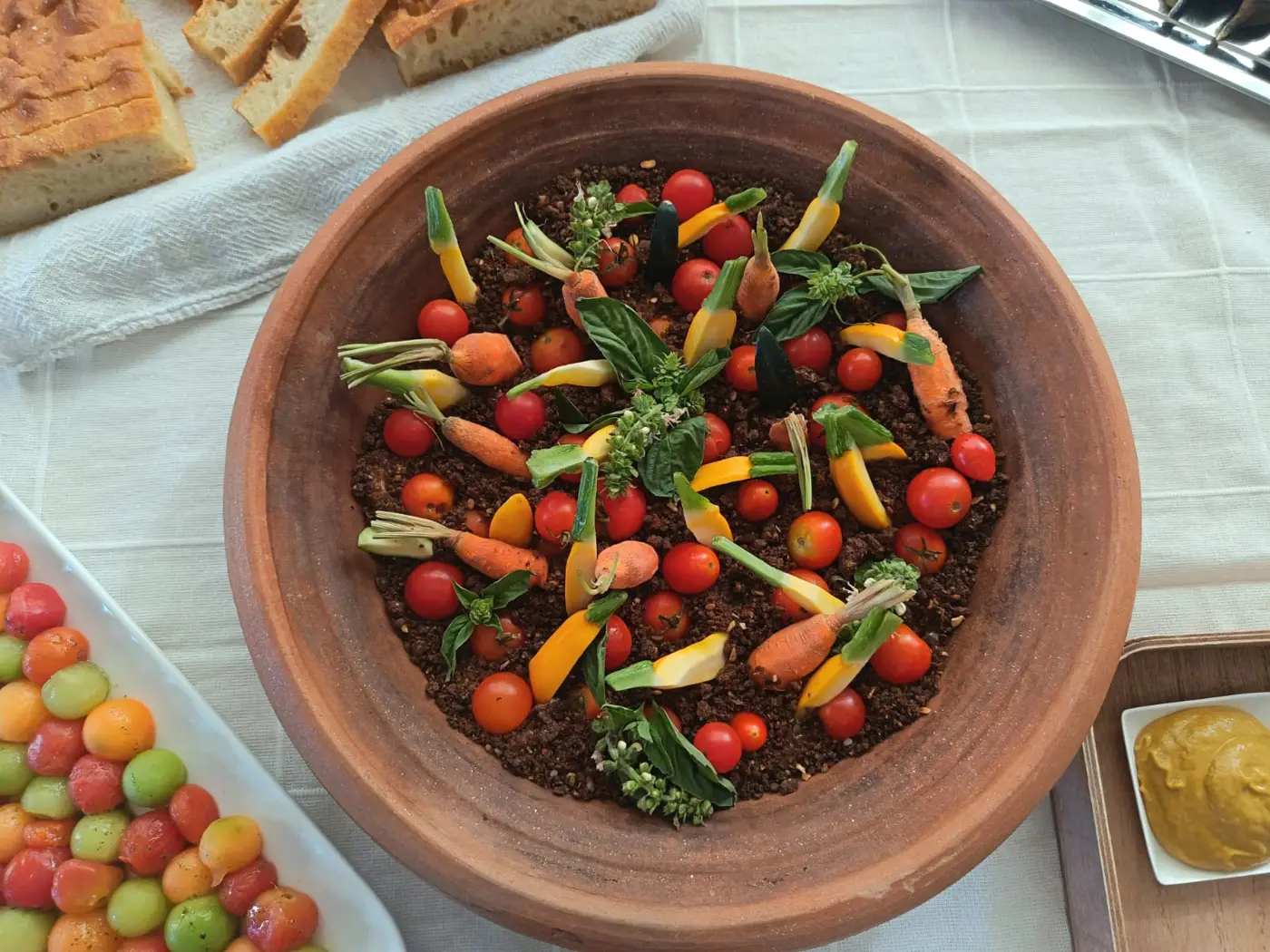 Bol en terre cuite garni de petites tomates, de carottes nouvelles et d'herbes, posé sur une nappe claire