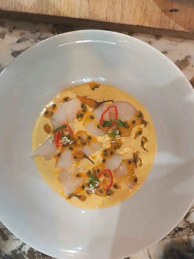 Fines tranches de poisson cru, sauce jaune, graines et piment dans une grande assiette blanche