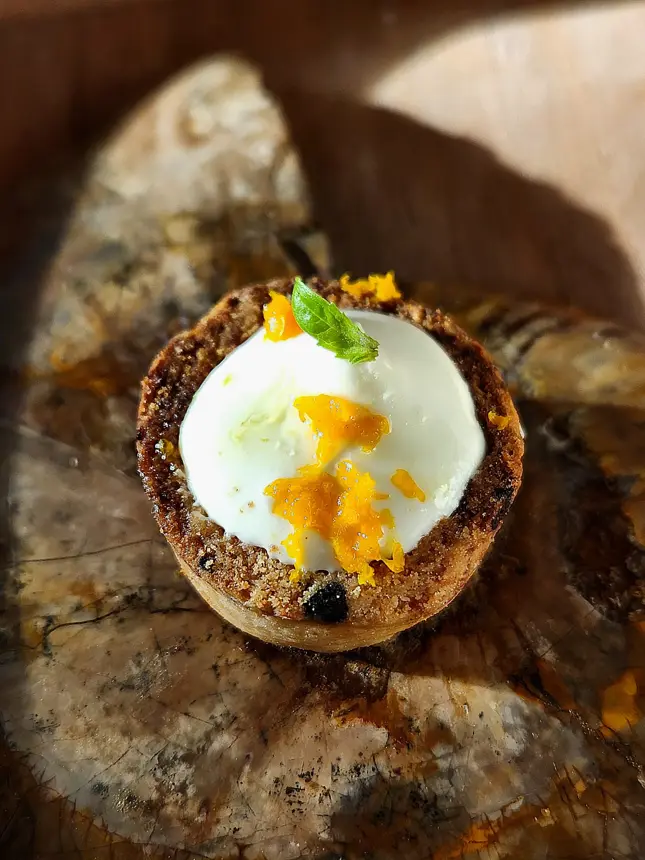 Dessert : boule de crème blanche, gel orange et croustillant sur fond sombre