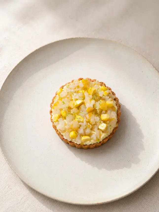 Tartelette à la garniture jaune sur une assiette claire très épurée